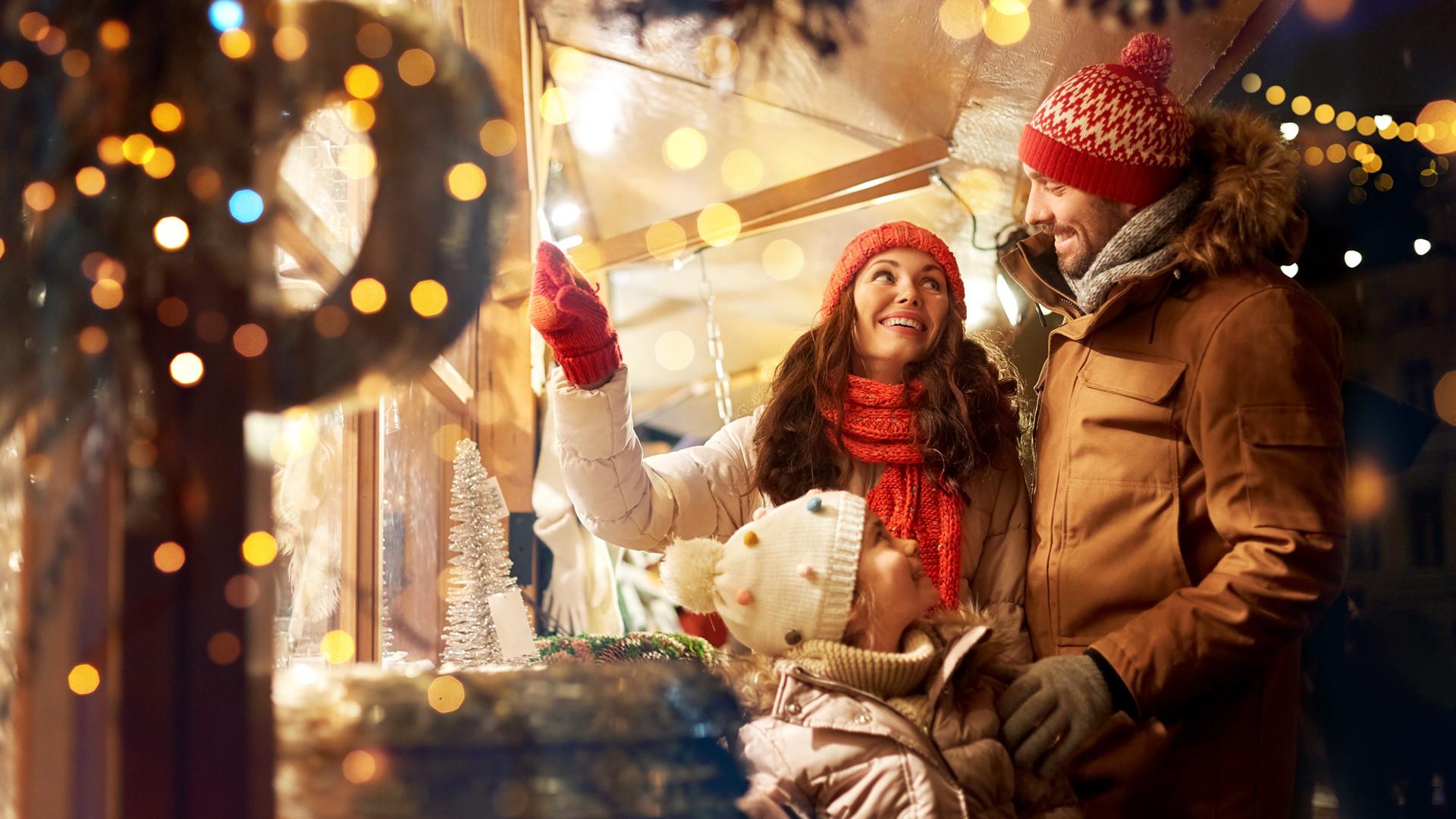 Famiglia felice che fa shopping natalizio al mercato, circondata da luci festive.